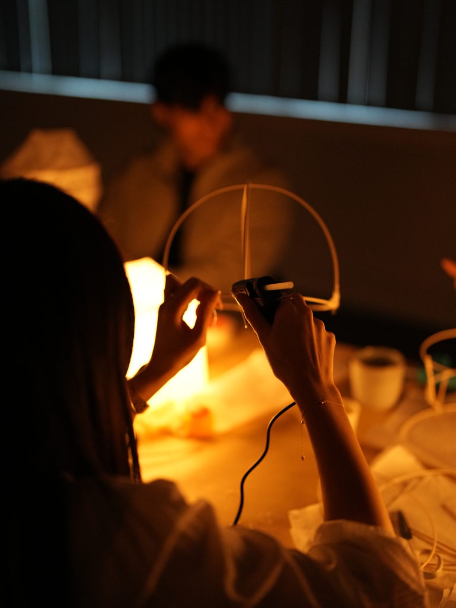 A participant gluing a bamboo rib into place on a half-built lamp frame.