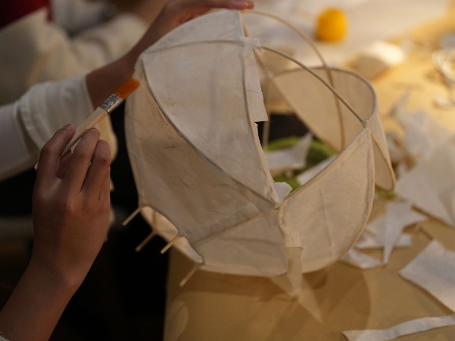Hands brushing paste along the paper seam of a lamp frame.
