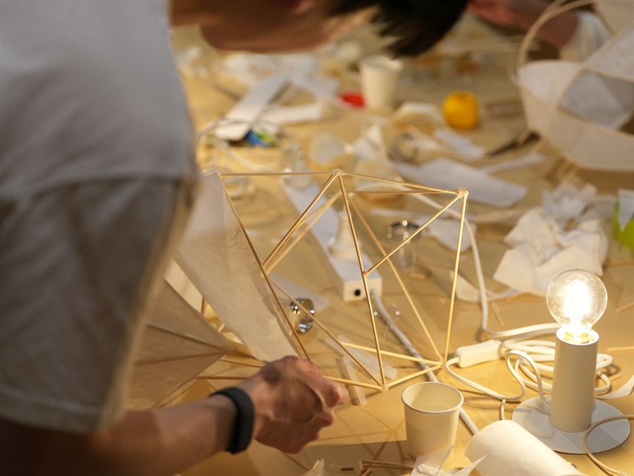 Participants building bamboo lamp frames together around a workshop table.