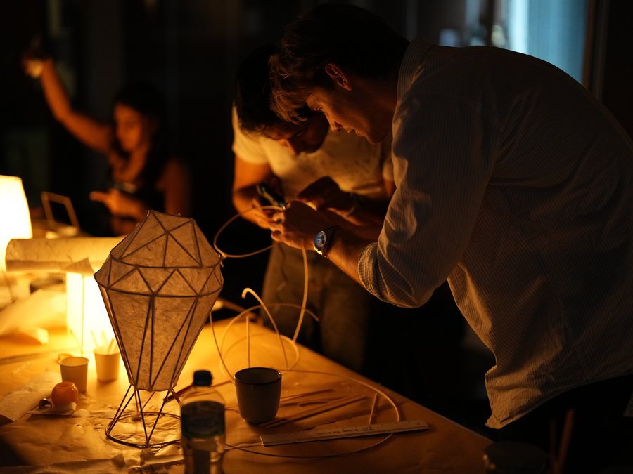 Workshop participants making paper lamps together around a warmly lit table.